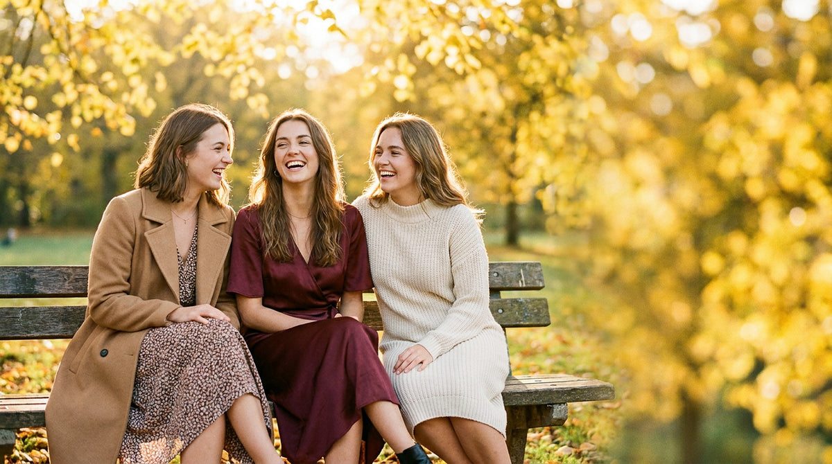 Three friends laughing on a park bench in fall