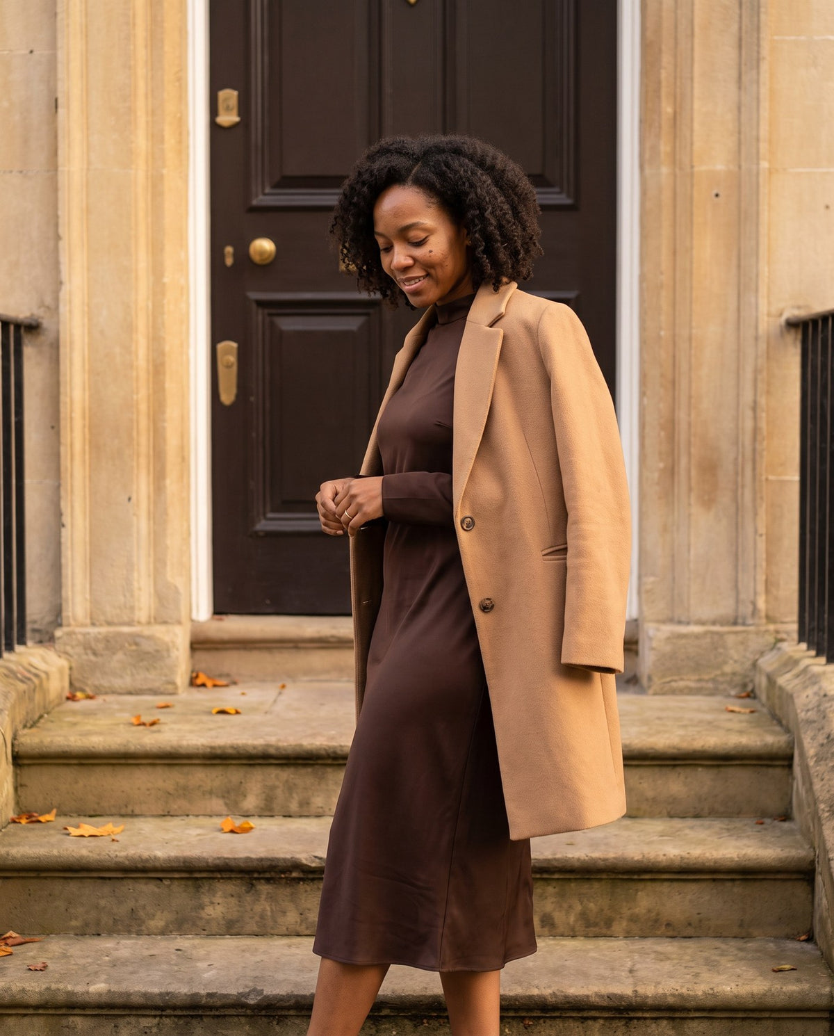Chocolate satin dress with a camel coat on townhouse steps